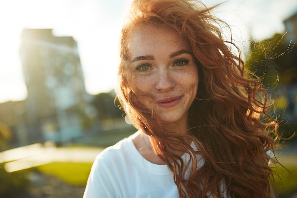 Portraits of a charming red-haired girl with a cute face. Girl posing for the camera in the city center. She has a wonderful mood and a lovely smile.