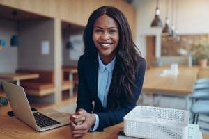 Smiling young African American businesswoman leaning on a table in an office lounge working on a laptop