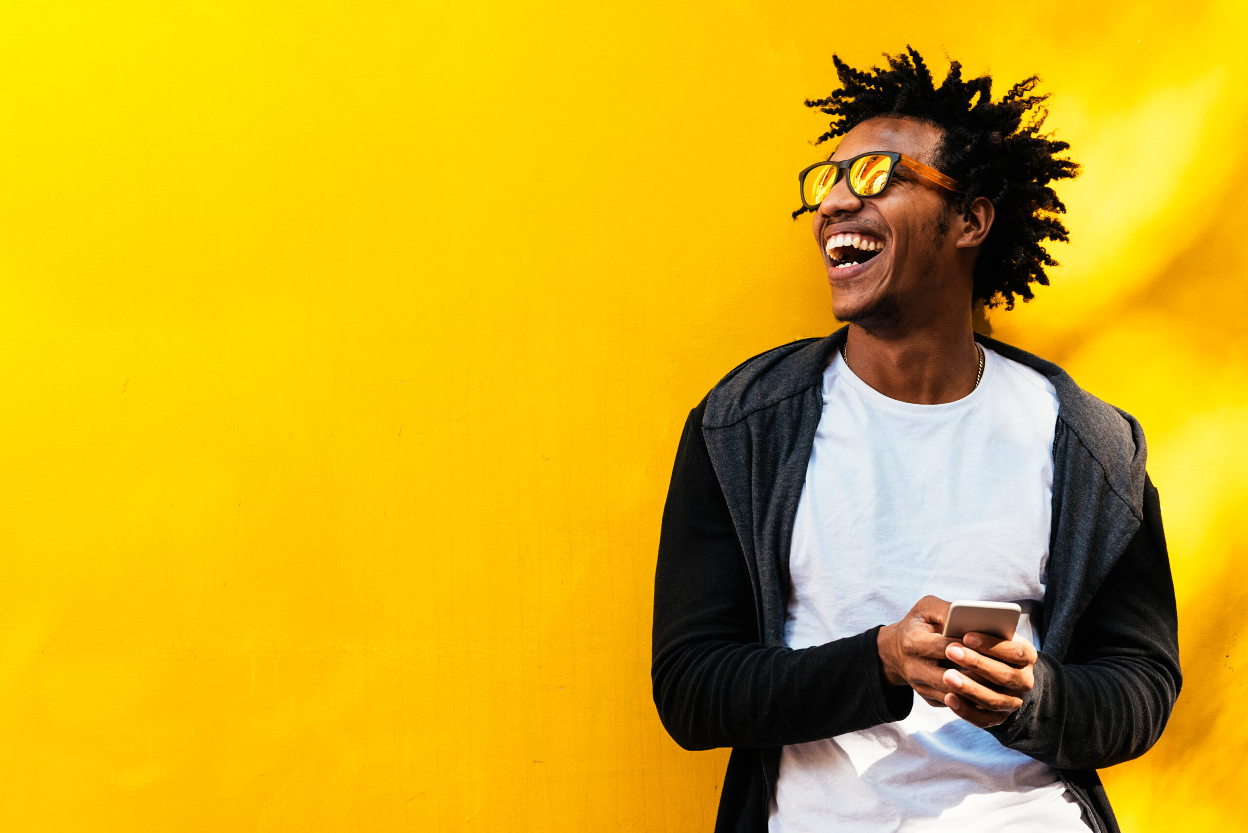 Man holding cellphone smiling on yellow background