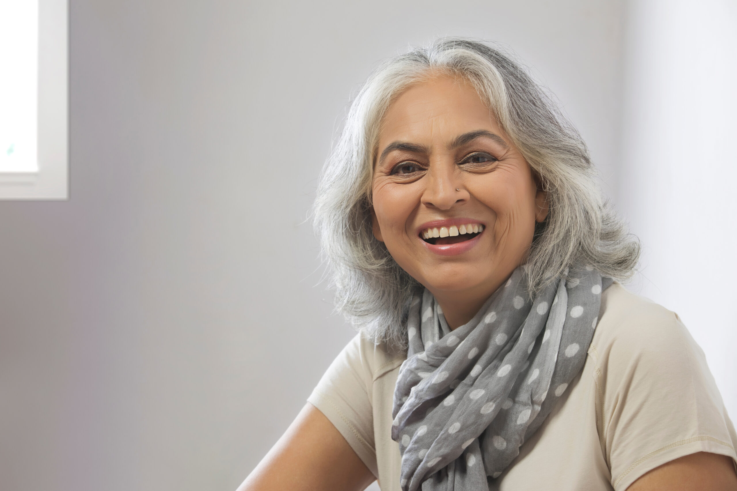 Woman with grey hair smiling on grey background