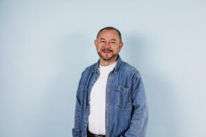 Latino man smiling in jean jacket and white shirt on blue background